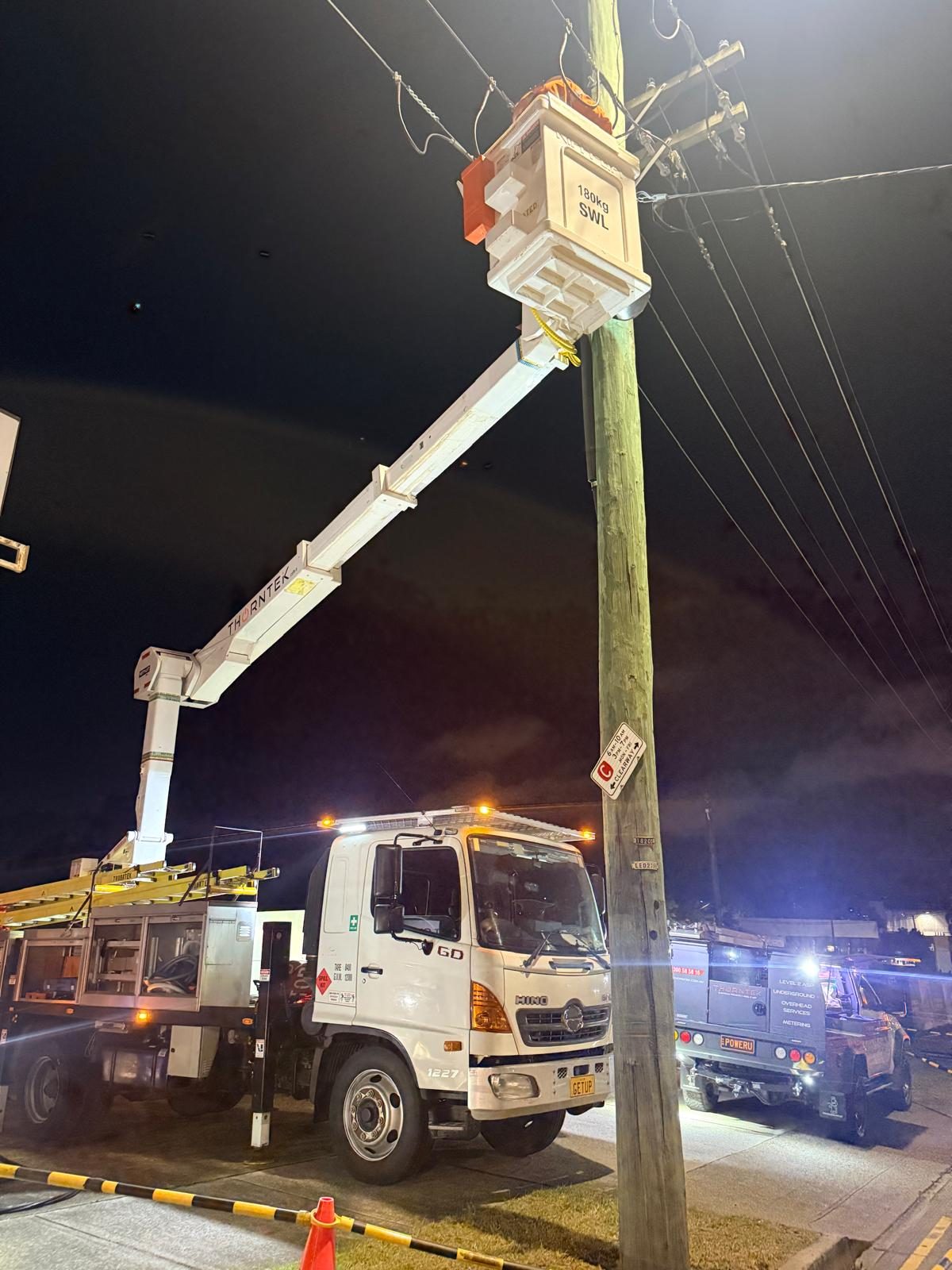 Thorntek elevated work platform at the top of a power pole at night, replacing overhead mains under traffic control