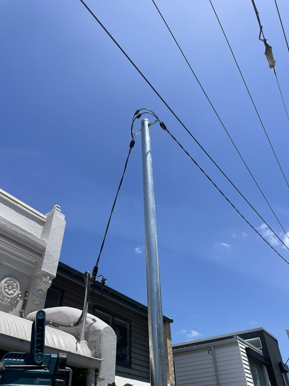 Top of a new steel private pole with the service mains and consumer mains connected, looking up from the street