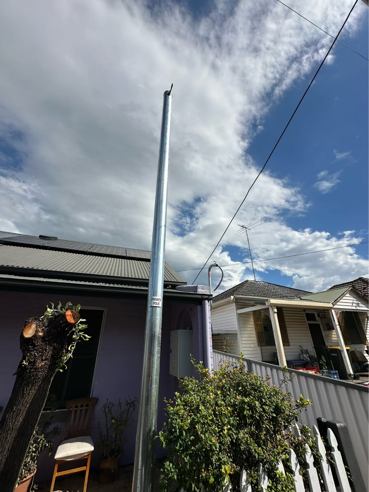 New galvanised steel private power pole with its private pole tag beside a weatherboard cottage